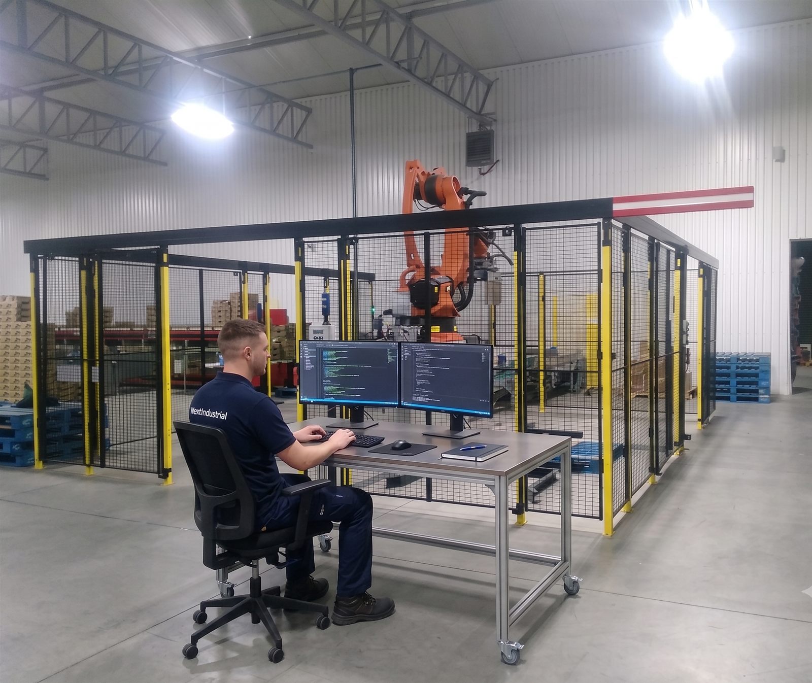 NextIndustrial-medewerker programmeert een robotcel met veiligheidshekwerk op de werkvloer